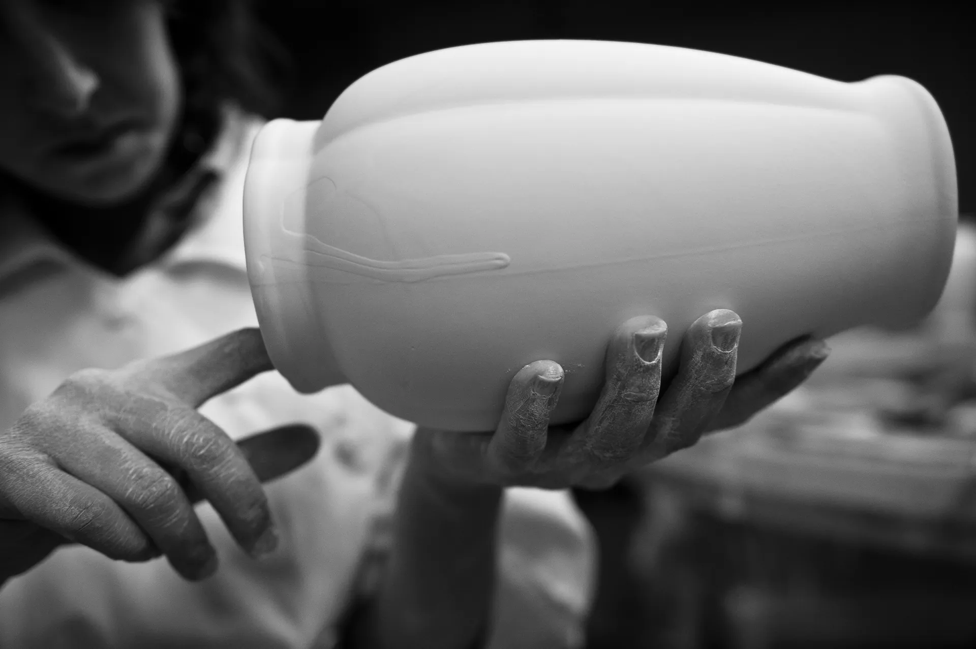 Main tenant une éponge polissant le bord d'une pièce en faïence, clair-obscur