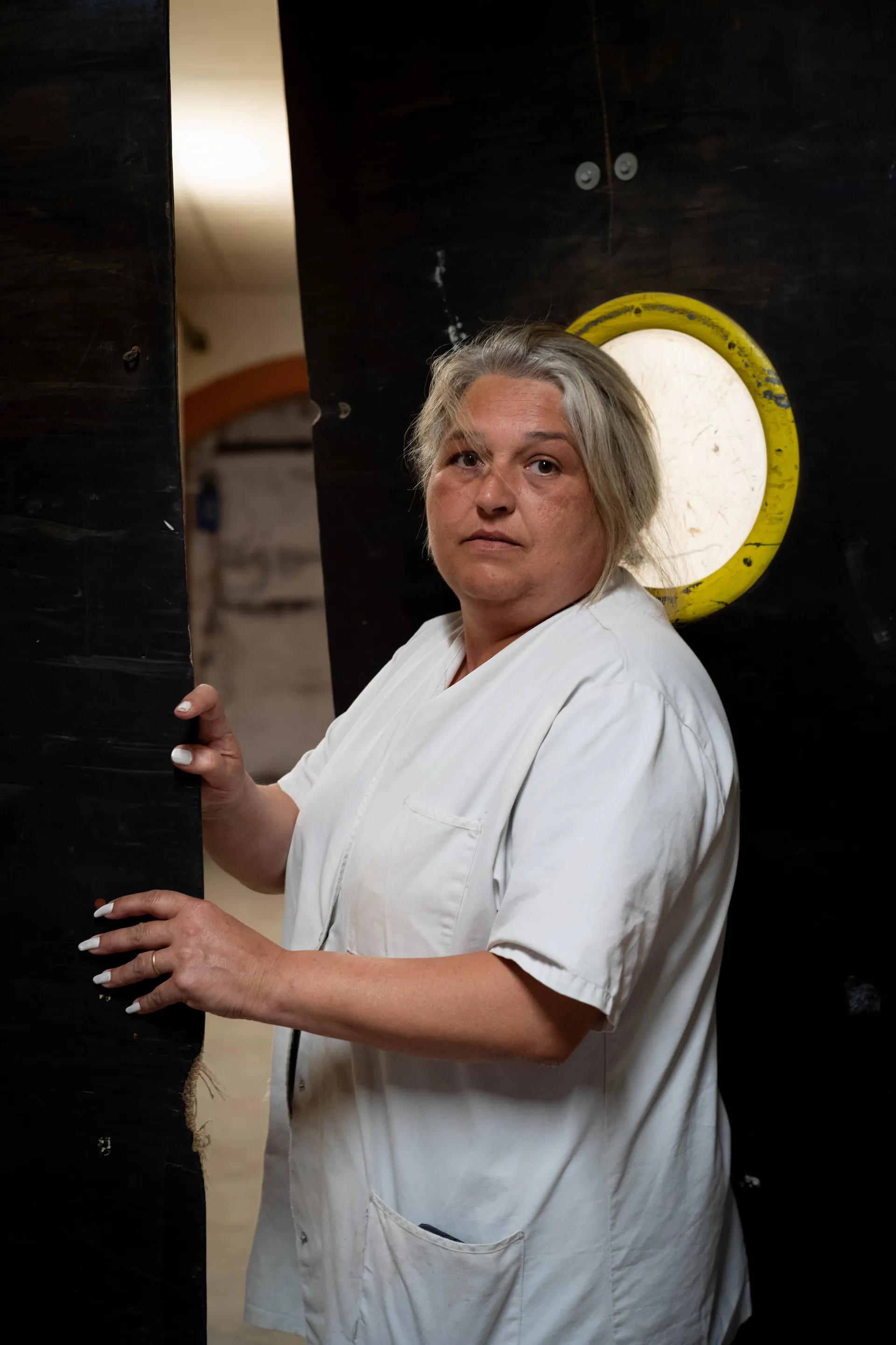 Portrait d'ouvrière en blouse blanche devant un mur industriel vert, regard frontal