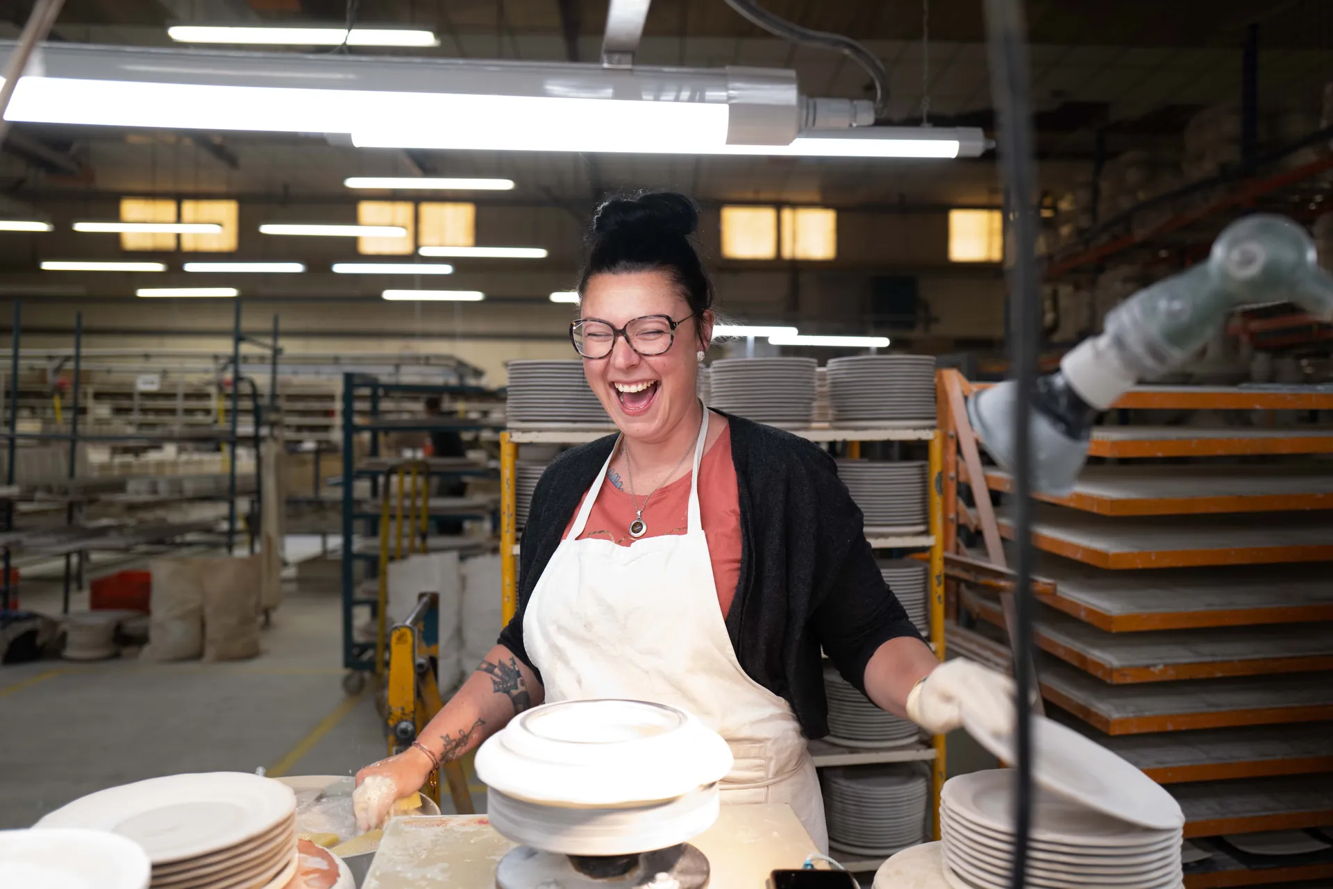Portrait rapproché d'une jeune ouvrière, cheveux courts, boucle d'oreille violette, atelier en arrière-plan