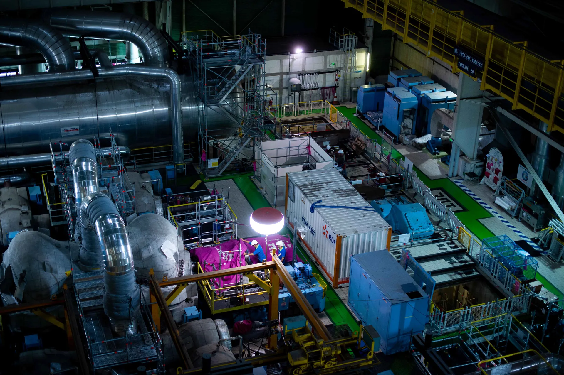 Vue plongeante sur la salle des machines d'une centrale nucléaire en maintenance, tuyauteries et échafaudages