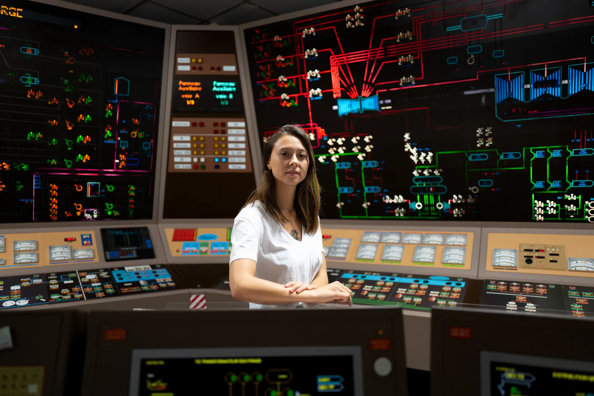 Opératrice posant bras croisés devant les synoptiques lumineux multicolores d'une salle de commande de centrale nucléaire