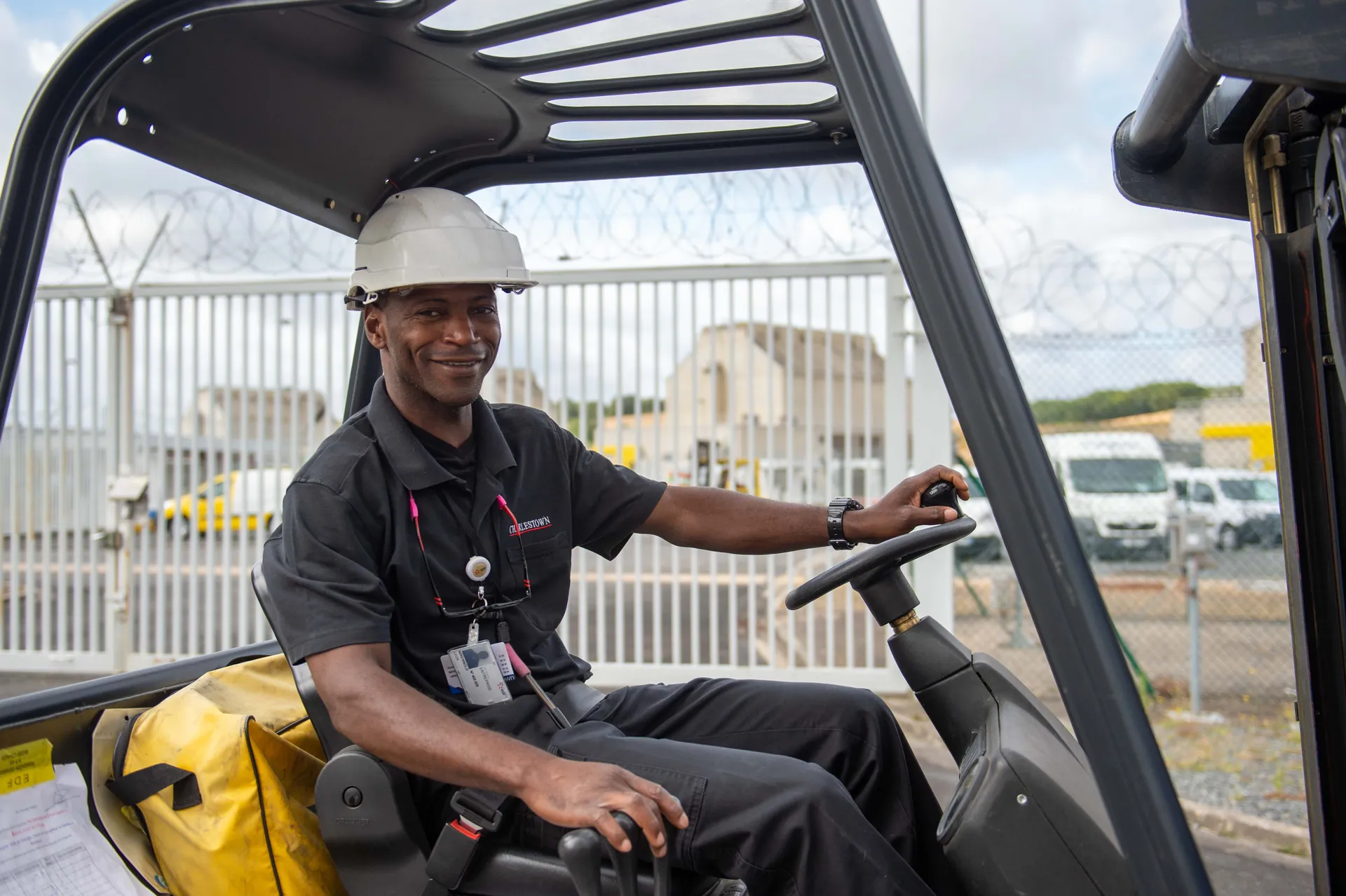 Cariste Charlestown souriant au volant de son chariot élévateur, casque blanc, sur le site d'une centrale nucléaire