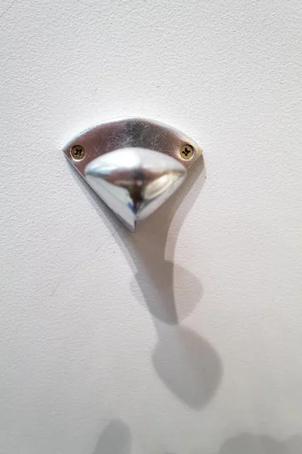 Crochet chrom&eacute; minimaliste sur mur blanc, ombre port&eacute;e