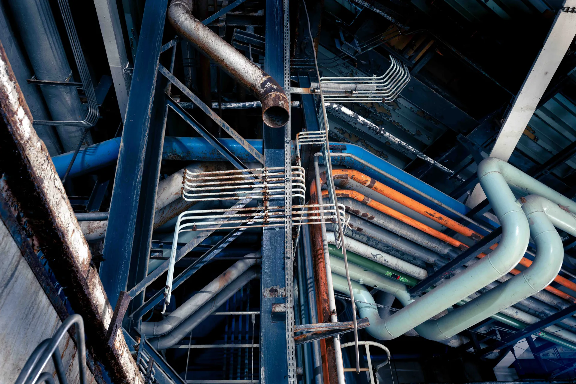 Faisceau de tuyaux sym&eacute;triques sur mur b&eacute;ton, grille m&eacute;tallique au sol