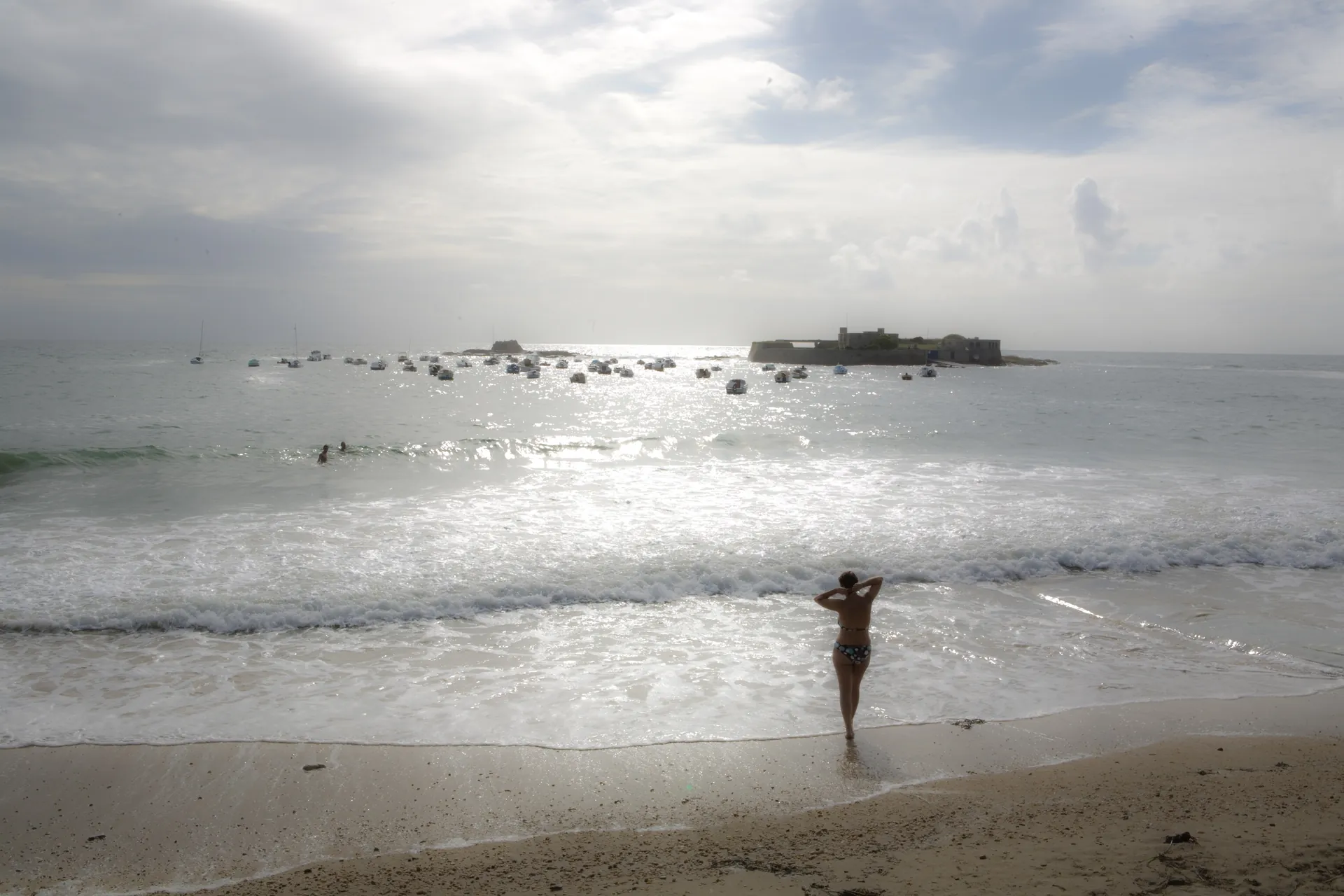 Enfant debout sur des rochers plats stratifiés face à l'océan, formations rocheuses imposantes