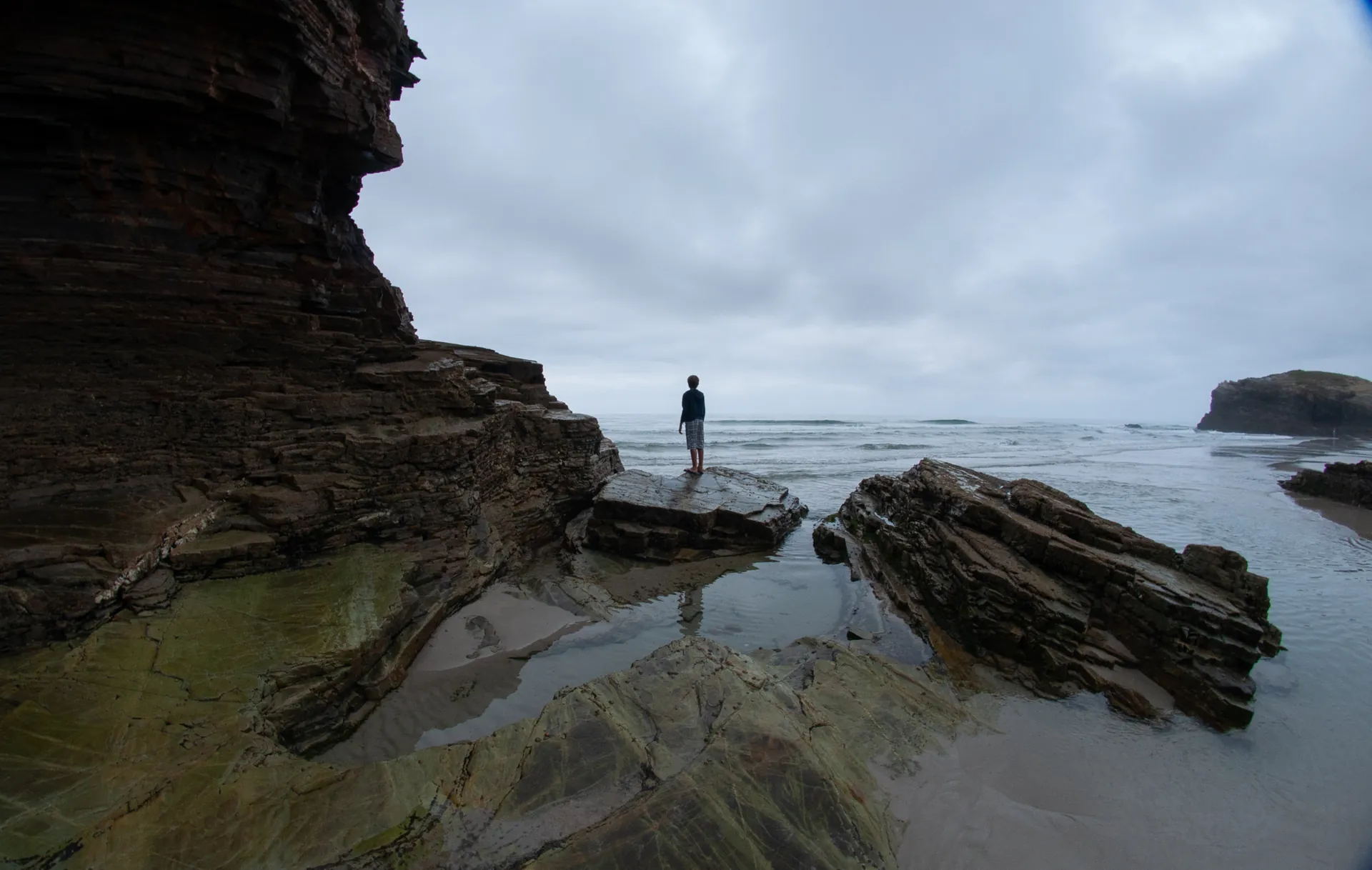 Couple penché sur un muret de pierre surplombant une plage, mer turquoise