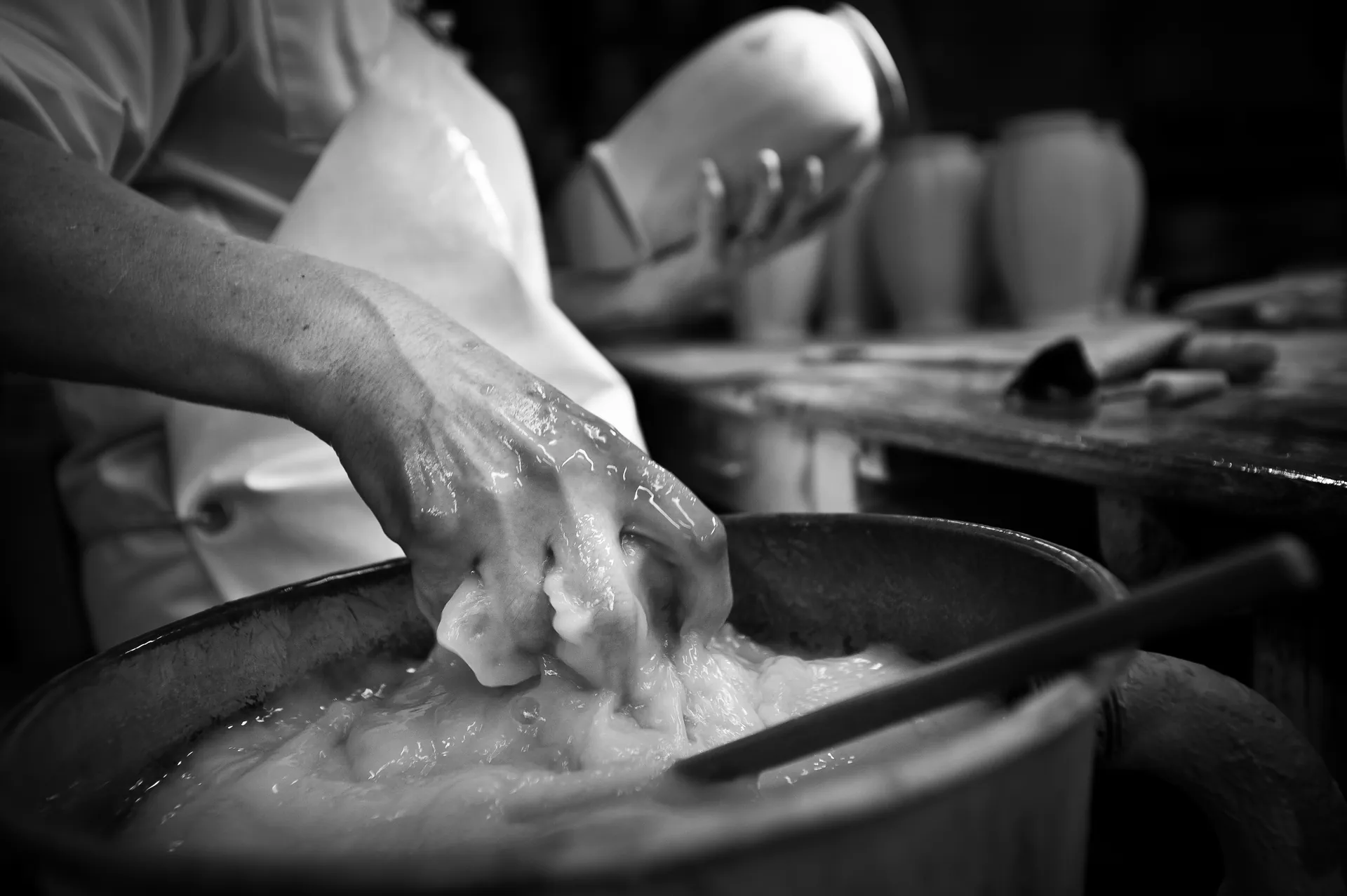 Main posée sur une pièce en terre crue sur un tour de potier, doigts marqués par l'argile