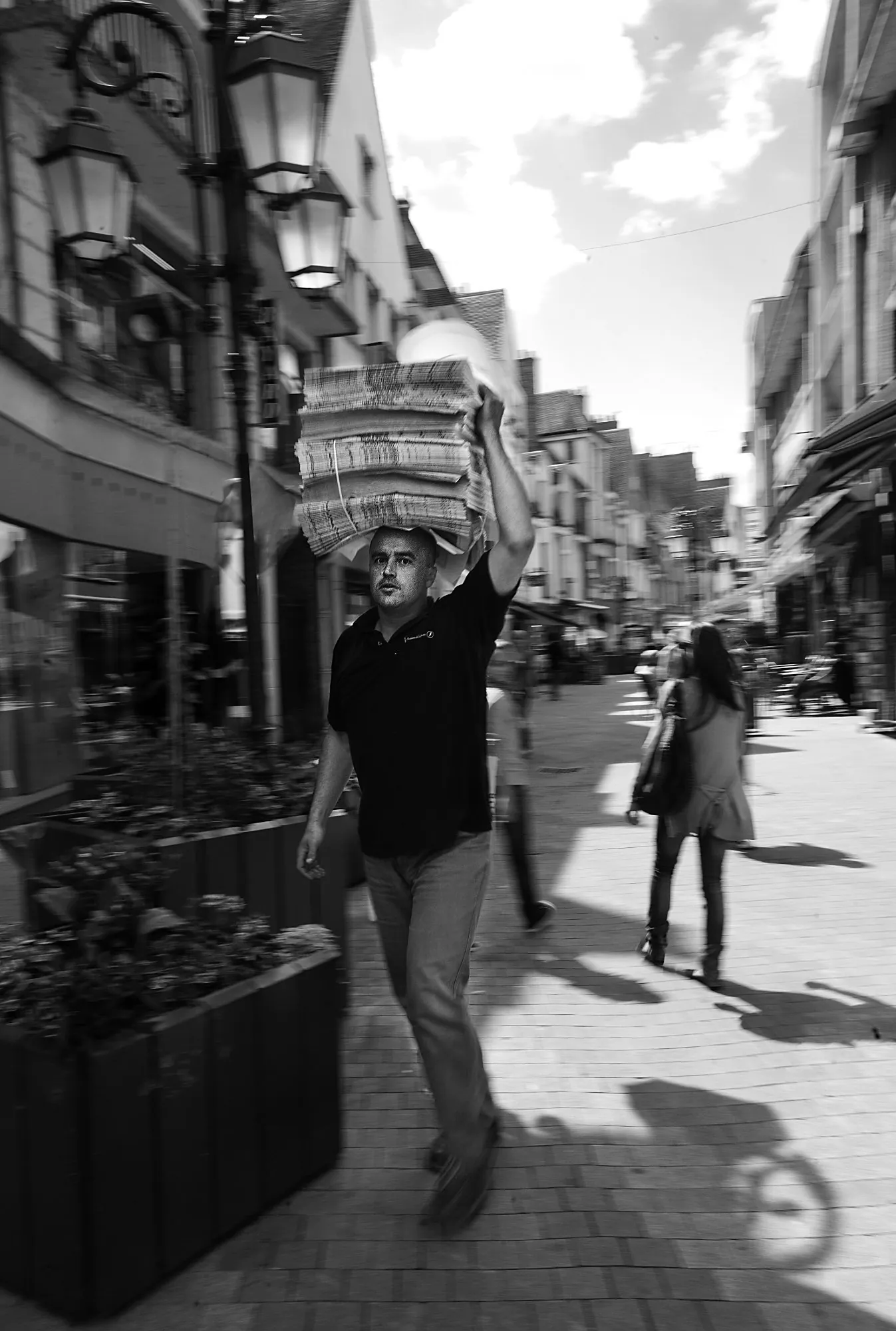 Distributeur portant une pile de journaux sur la tête dans une rue piétonne de Gien