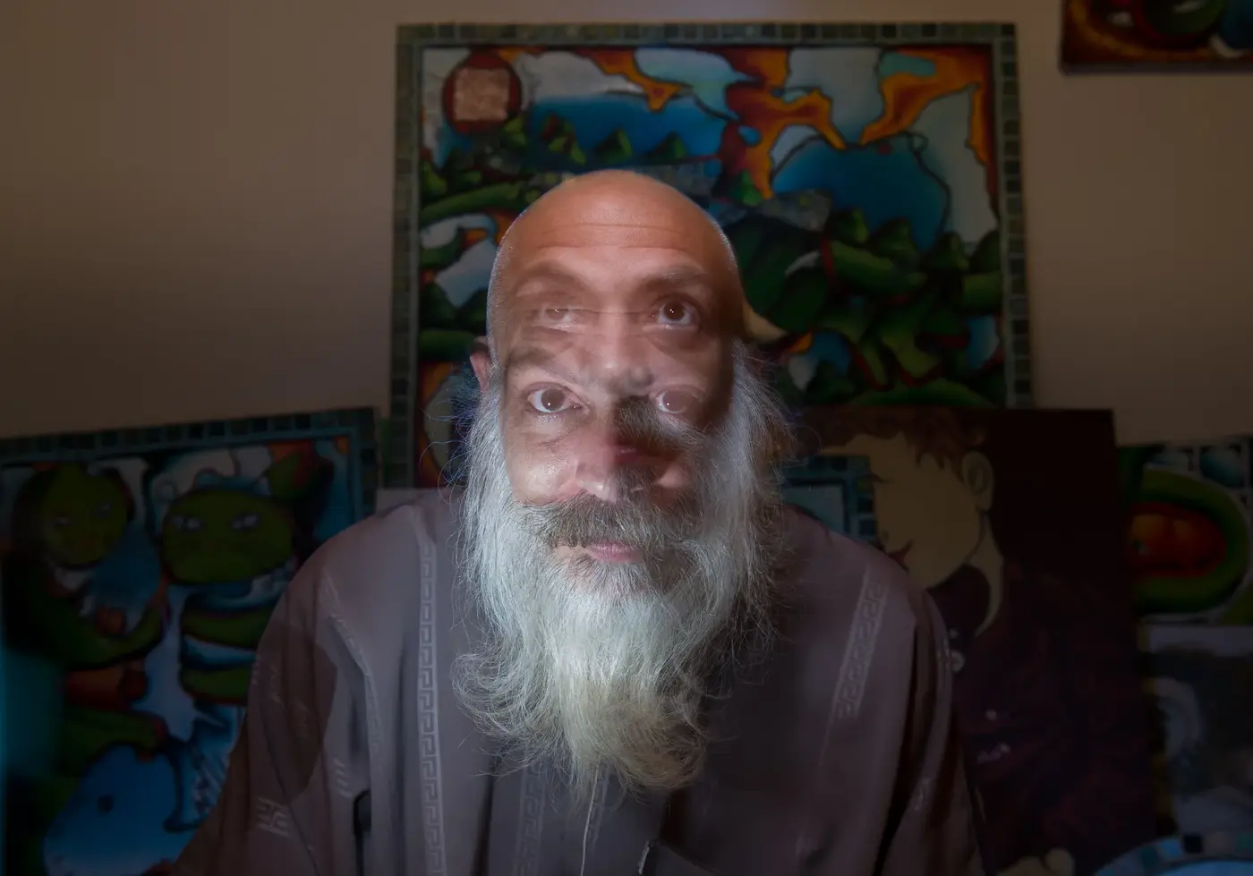 Artiste au crâne rasé et barbe blanche assis devant ses toiles colorées dans son atelier