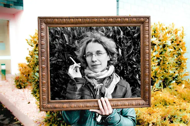 Anne-Laure Bondoux, autrice, tenant un cadre doré, intérieur noir et blanc, extérieur couleur